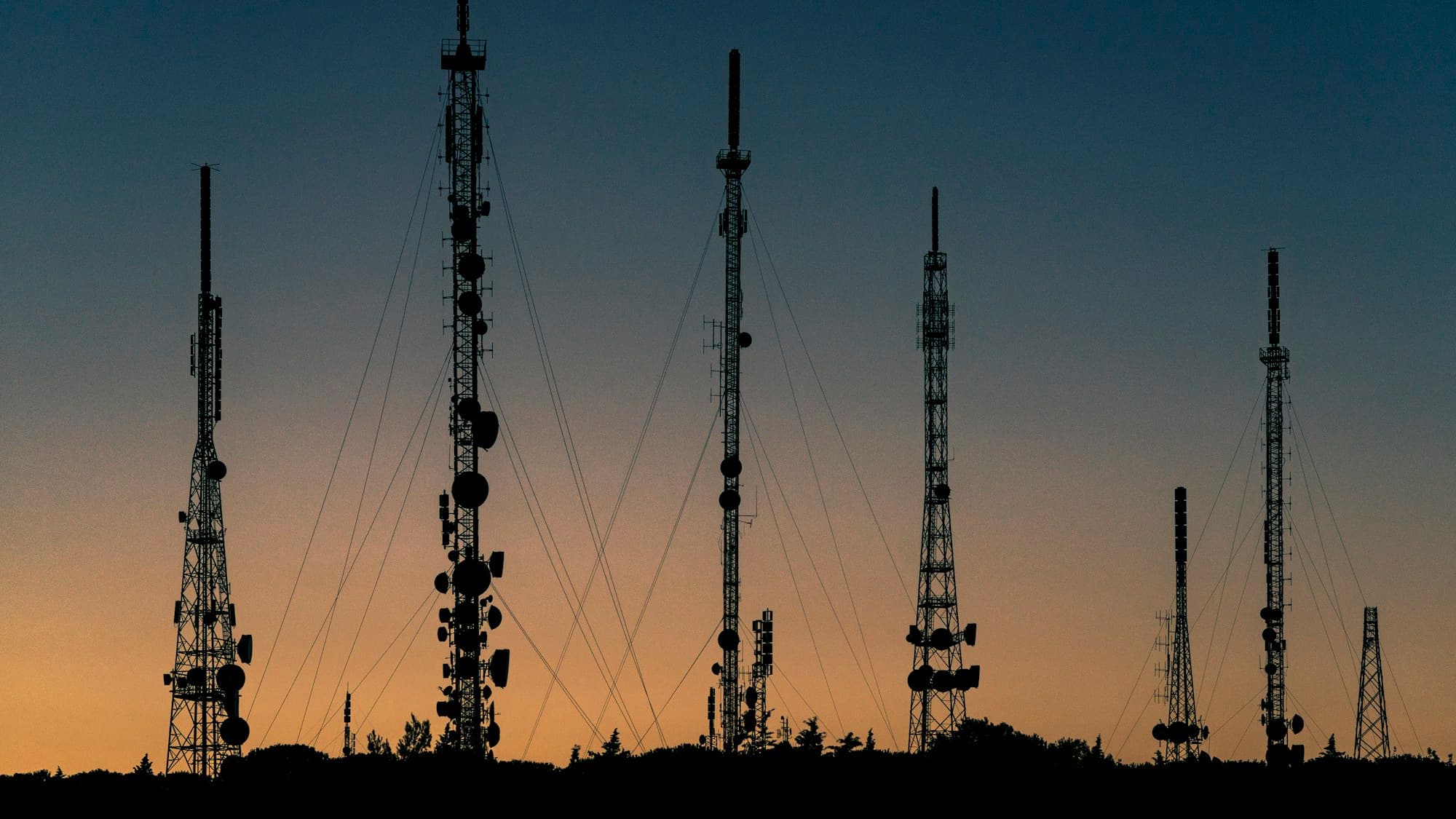 Silhouetted communications towers against a dusk sky